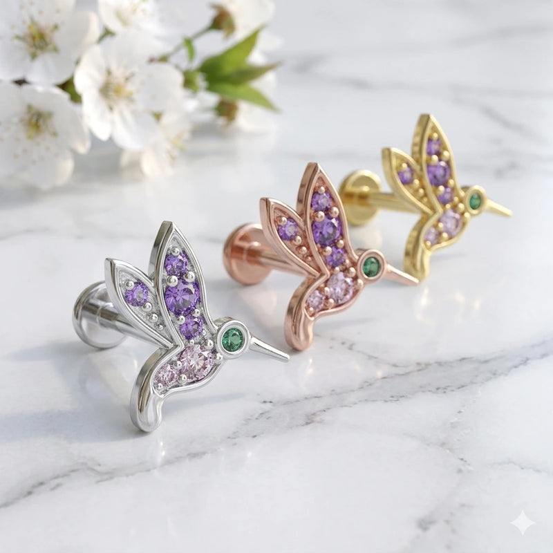 Hummingbird flat back earrings in 14K white, rose, and yellow gold with gemstones beside spring blossoms