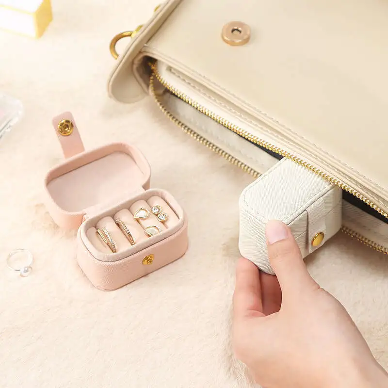 Compact travel jewelry box shown open with rings inside and slipped into a handbag for portability