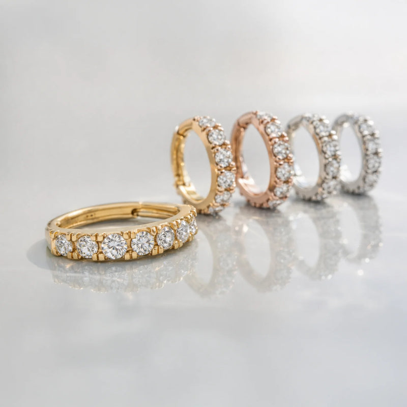 CZ infinity clicker hoop in 14k yellow, rose, and white gold variants lined up on reflective surface