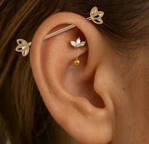 14k gold lotus industrial barbell shown in model's cartilage piercing for fit and scale