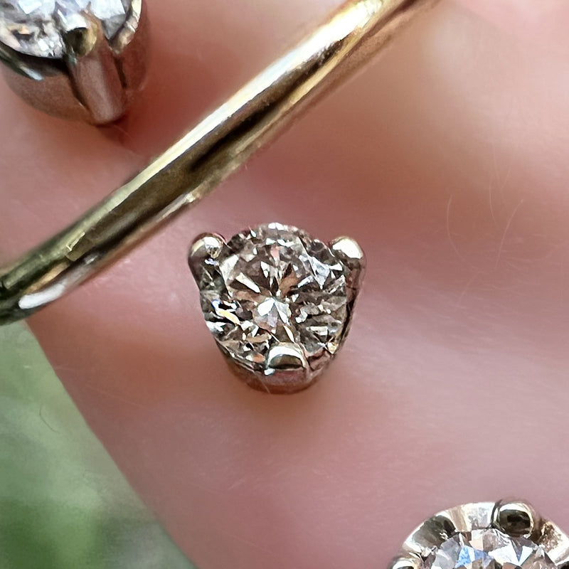 Extreme close-up of 3-prong VS1 diamond setting resting on fingertip, showing facets and prong detail