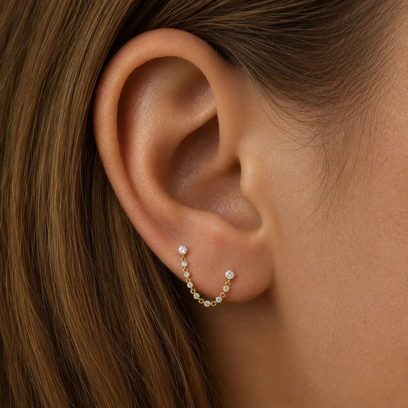 14K yellow gold Lyra CZ connector studs linking two ear piercings with draped gem chain on model