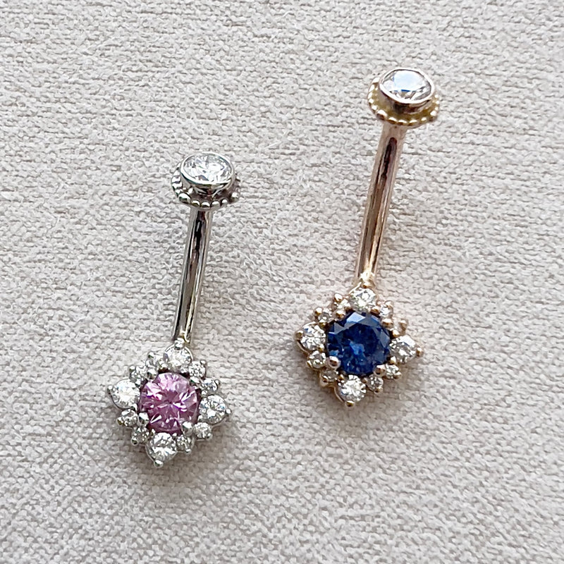 Two 14k gold halo navel rings side by side: white gold with pink sapphire and yellow gold with blue sapphire