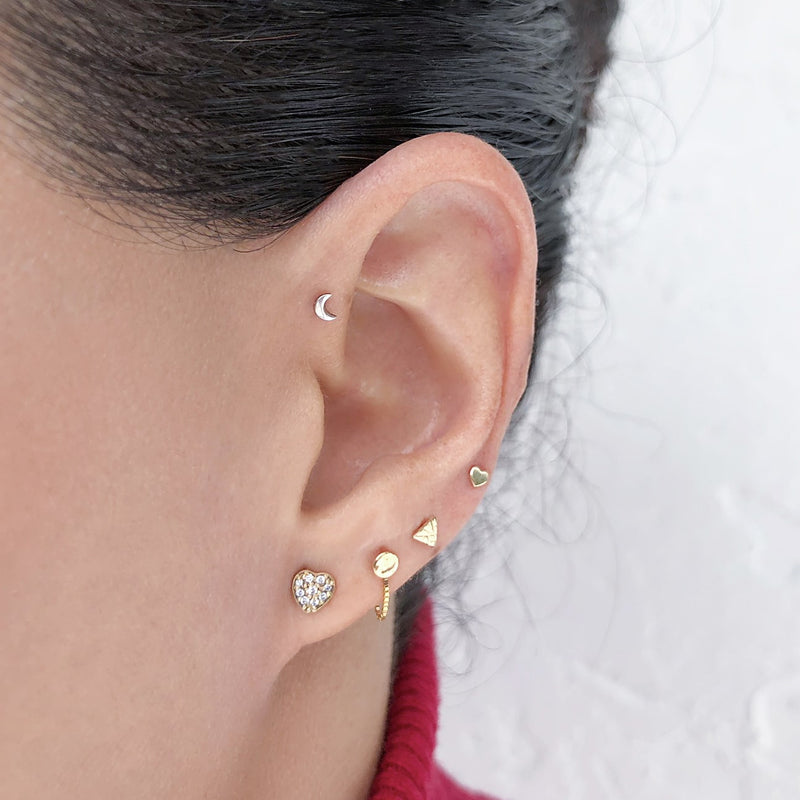 14k gold tiny heart flat back stud worn in upper lobe cartilage piercing on model's ear