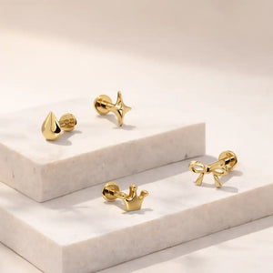 14k yellow gold crown labret stud grouped with star, bow, and droplet flat back studs on marble tile