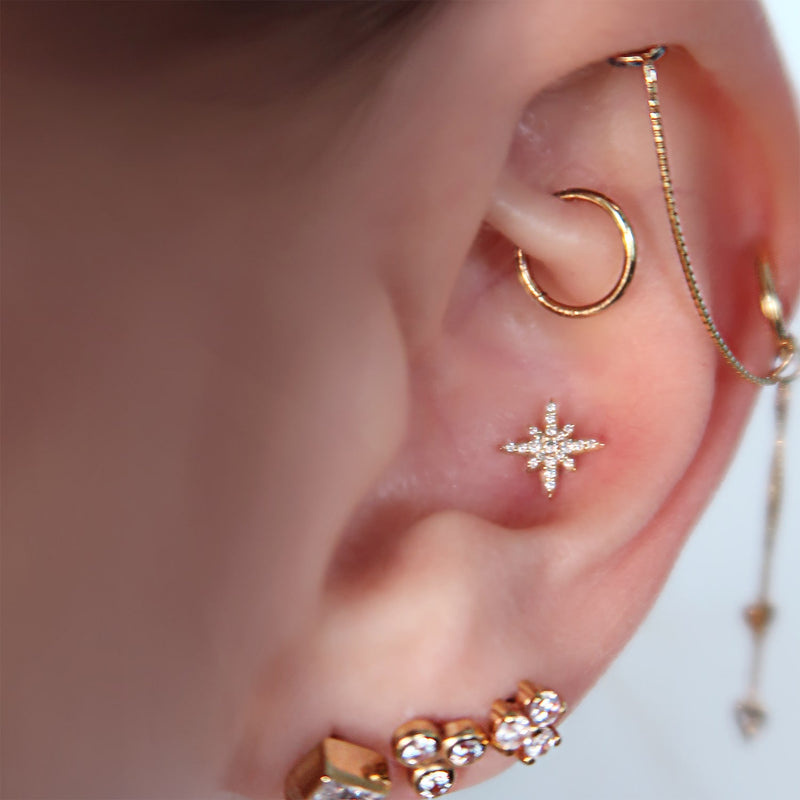 Diamond north star flat back cartilage stud shown in helix piercing, styled with gold ear stack