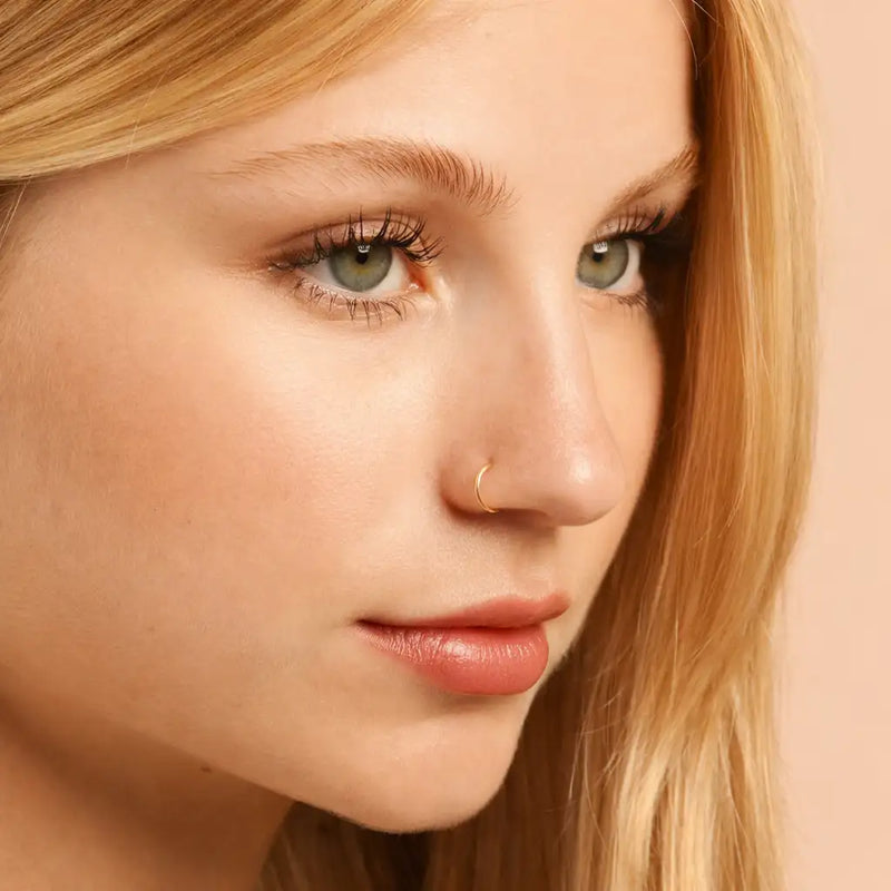 18K yellow gold seam ring hoop worn as nose ring on model, angled face view showing subtle fit