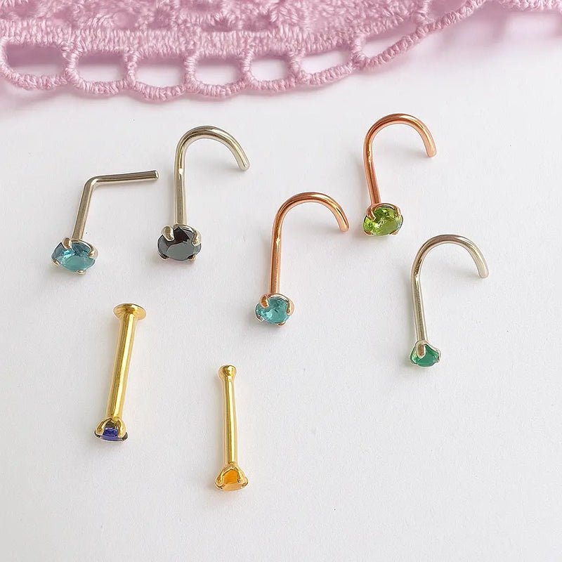 Flat lay of assorted gold nose rings in twist, L-shape, and bone styles with multicolor gemstones