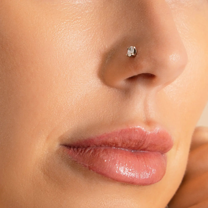 Oval diamond nose ring in white gold worn in nostril piercing, closer angled view on model
