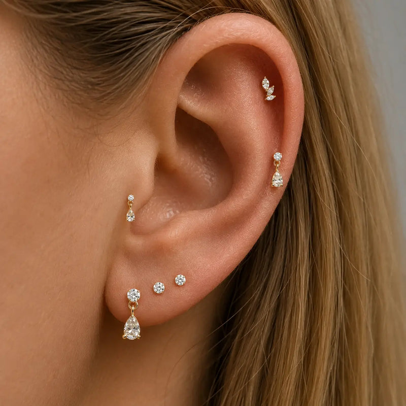 Close-up of an ear wearing multiple gold and diamond earrings against a neutral background