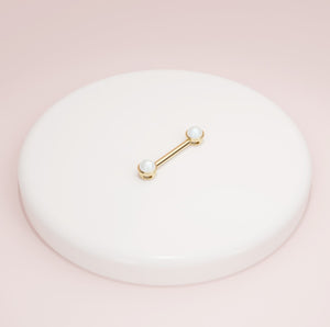 14K yellow gold pearl nipple barbell resting on white ceramic dish against pink background