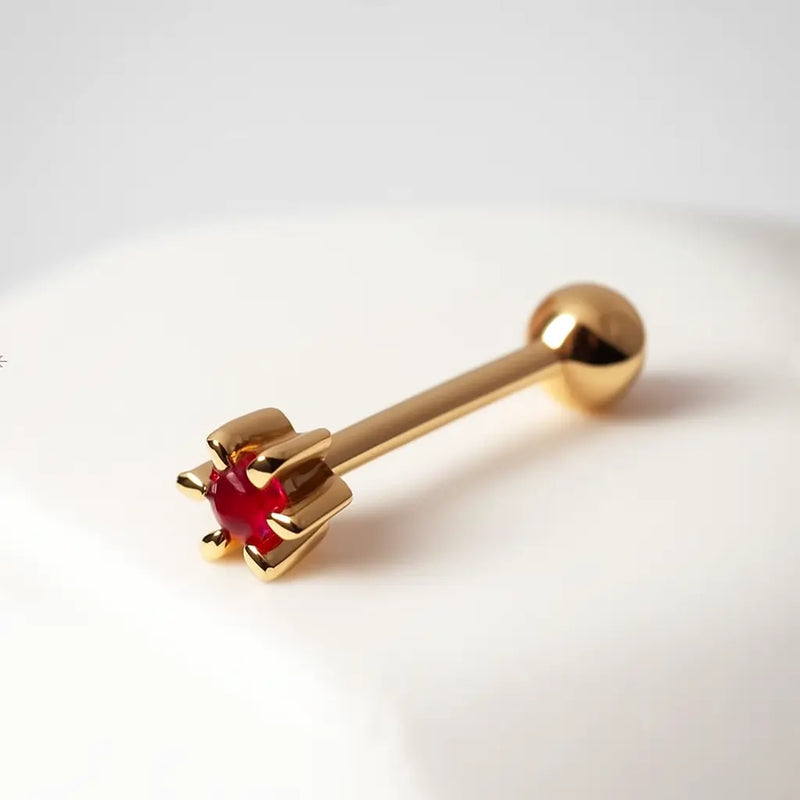 14k yellow gold flower cartilage stud with ruby gemstone, angled lifestyle view on white surface