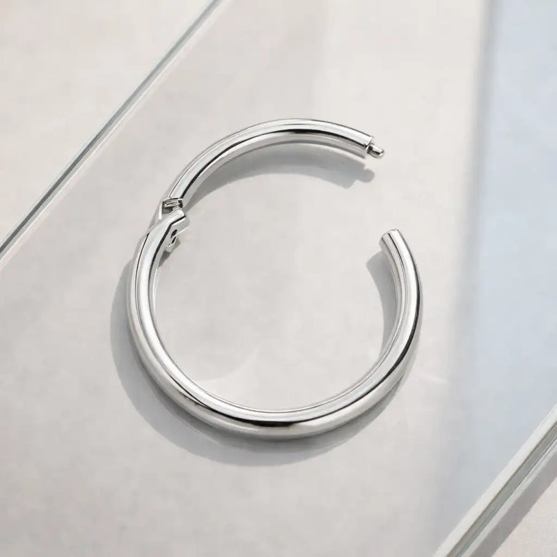 Platinum clicker ring hoop shown open on frosted glass surface, revealing hinge mechanism