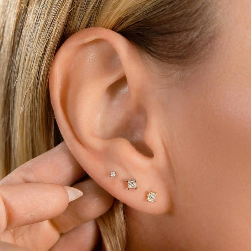 Princess-cut diamond flat back studs worn in triple lobe piercing stack on model's ear