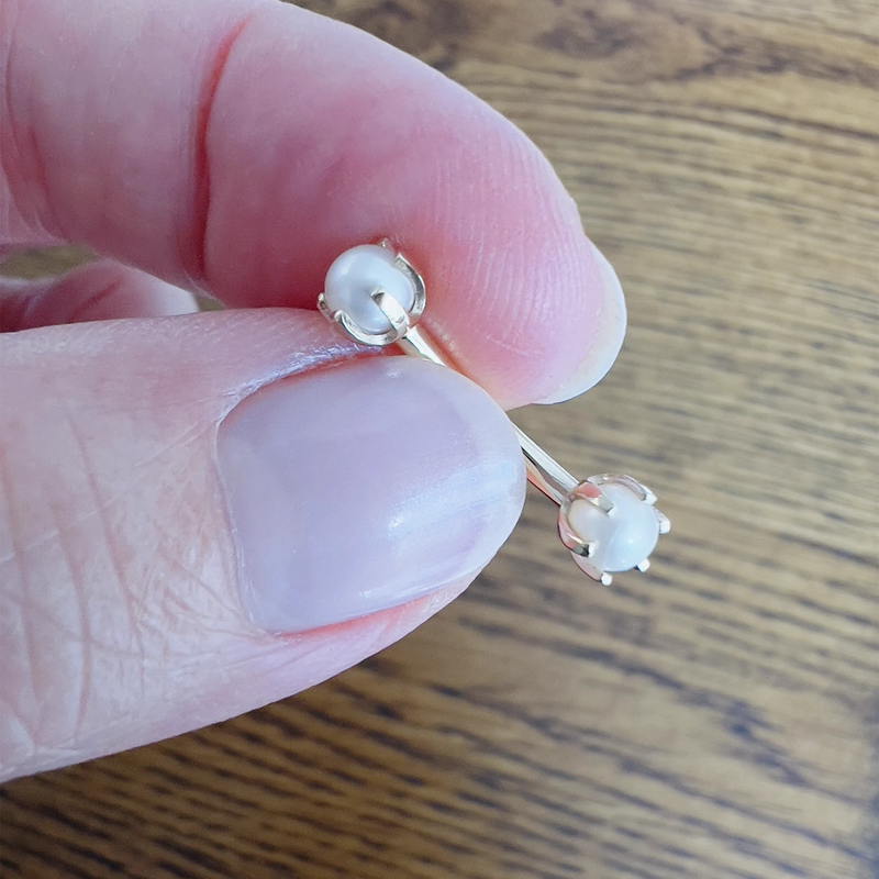 Pearl prong-set curved barbell held between fingers for size reference, silver tone