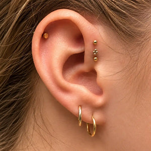 Close-up of an ear styled with a gold bead cluster stud, ball labret flat backs, a disc helix stud and two gold hoops