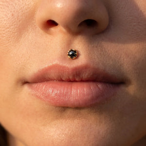 Close-up of a person's nose and lips wearing a small gold stud with a dark round gemstone in the medusa.