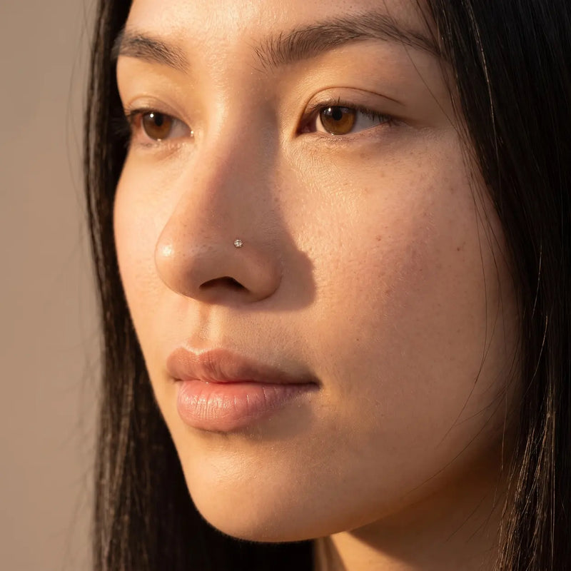 2.5mm Reina rose cut diamond nose ring in 14k yellow gold worn in a nostril piercing, close-up on a model