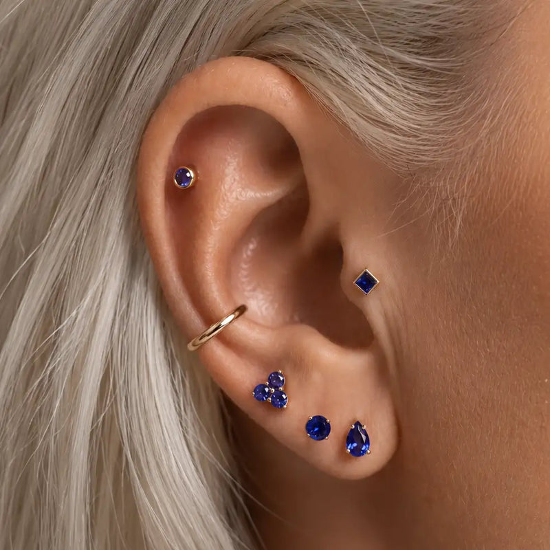 Close-up of a person's ear wearing multiple sapphire ear piercings and a gold hoop earring.