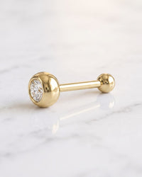 Tongue rings - 14k yellow gold tongue ring with a bezel-set diamond end and a plain gold ball end on white marble