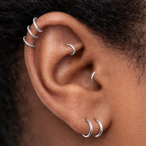 Platinum seam ring hoops stacked in helix, cartilage, and lobe piercings on model's ear