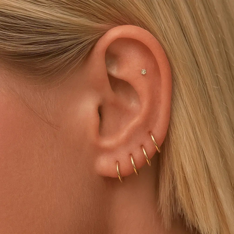 Multiple 18K yellow gold clicker hoops stacked across lobe and cartilage piercings on model's ear
