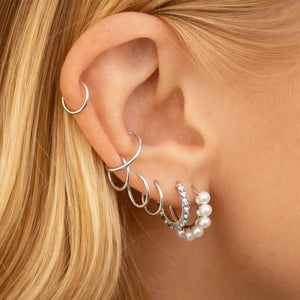 Platinum seam ring hoops styled in helix and flat cartilage piercings on model's ear, curated look