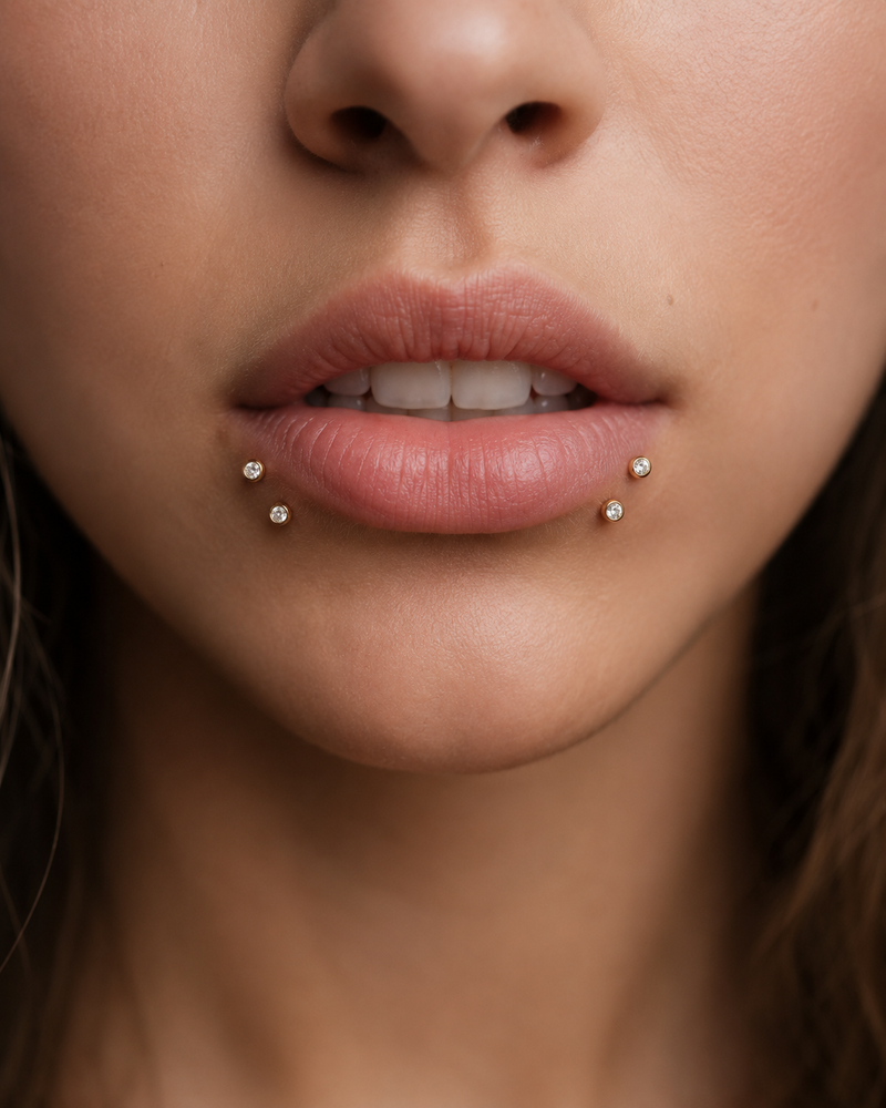 Shark bites piercing with four gold bezel-set studs, two either side of the lower lip