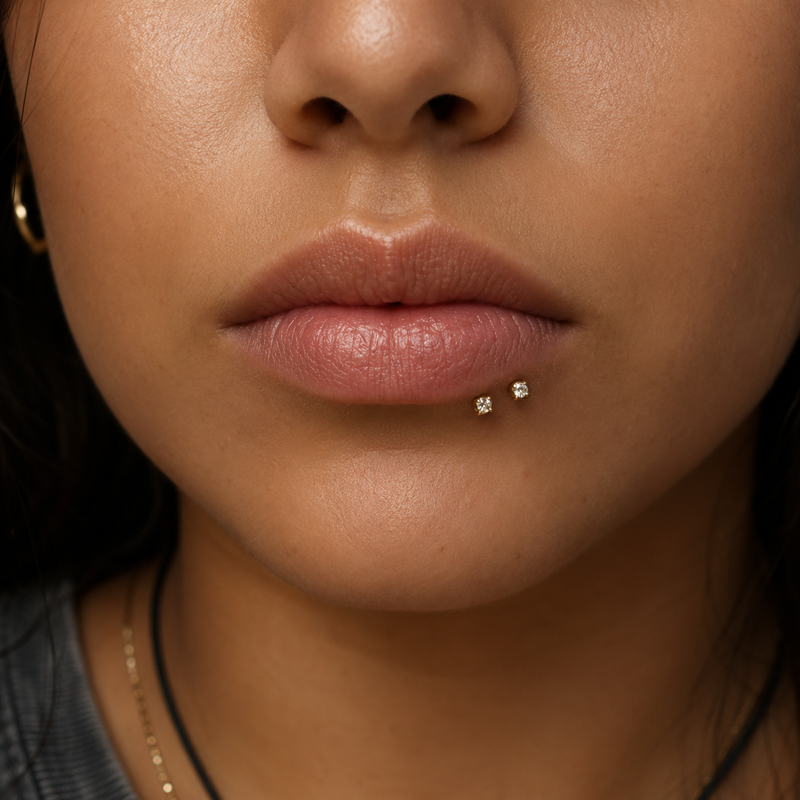 Spider bites piercing with two gold prong-set studs set close together on one side of the lower lip