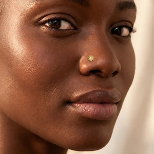 Close-up of a person's face wearing the Surya's Fire nose stud against a soft beige background.