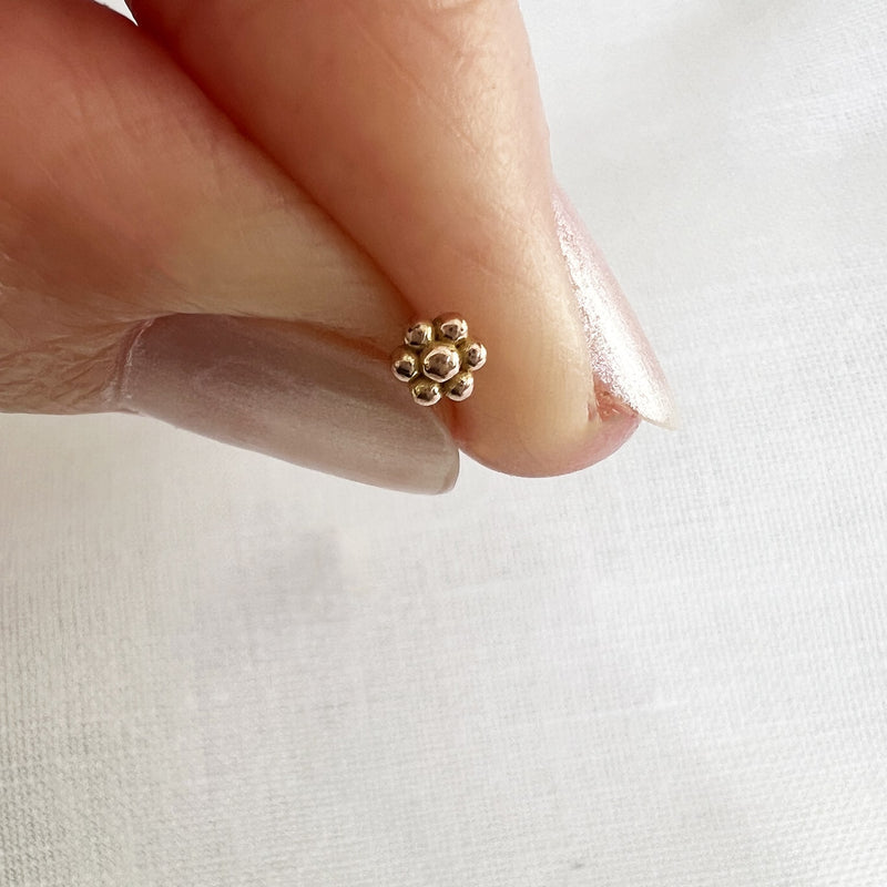 Tiny 14k yellow gold flower threadless end held between fingers for size reference