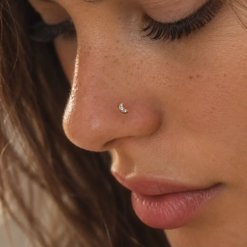 Close-up of a woman's nose wearing a small crescent moon stud with tiny clear gemstones.