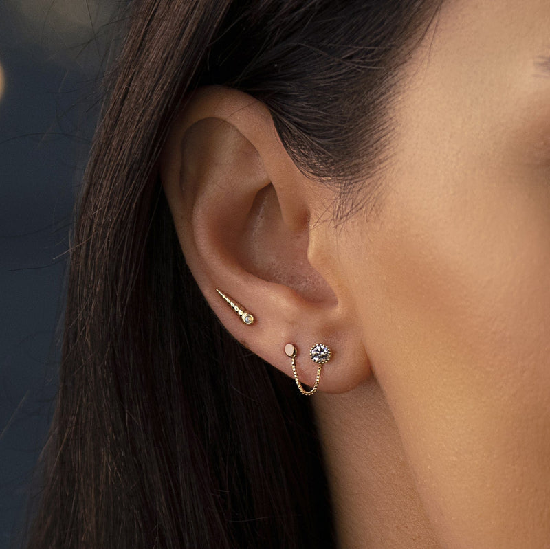 14K yellow gold tiny disc labret shown in tragus piercing, styled with chain and CZ earrings on model