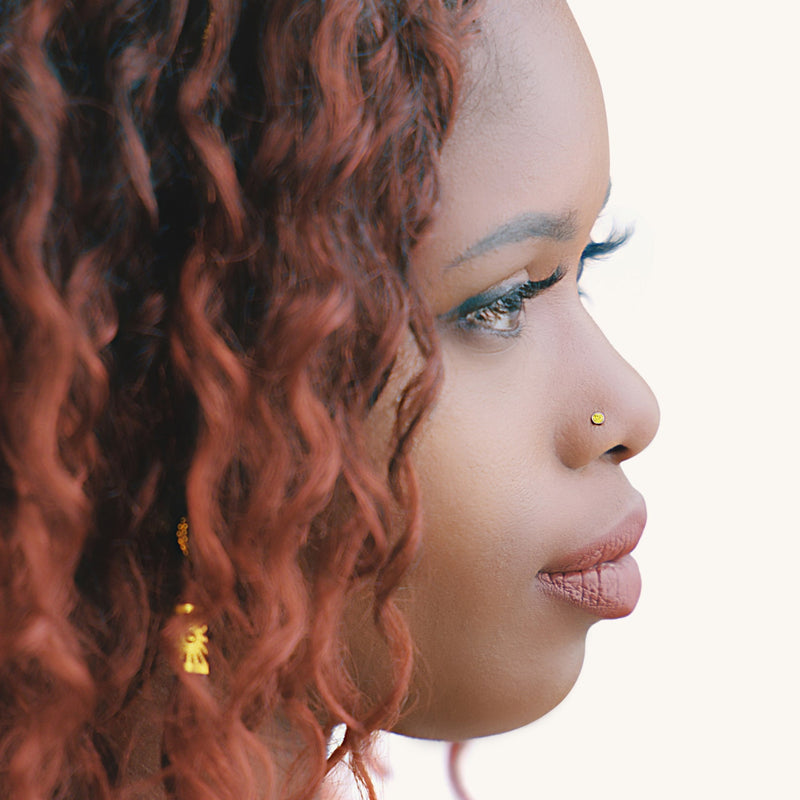 Yellow diamond bezel nose stud shown in pierced nostril on model, side profile view