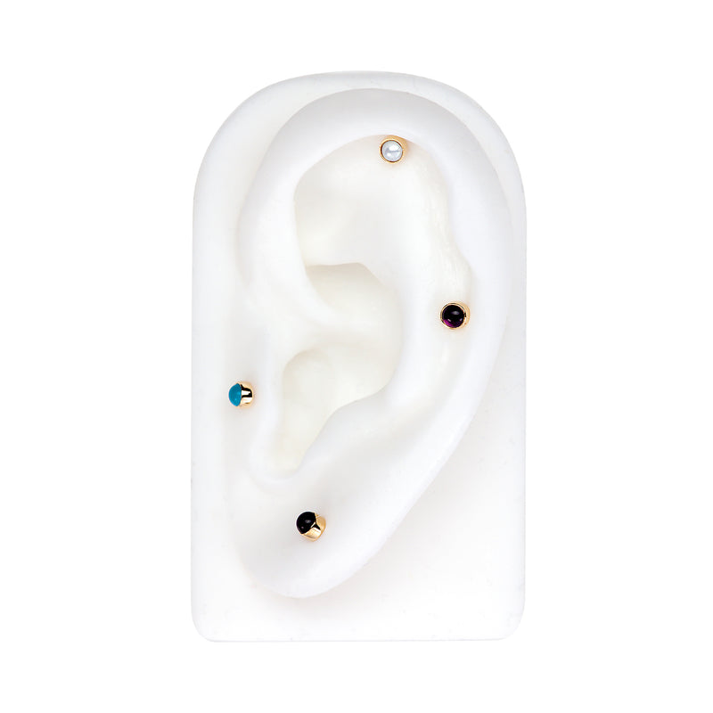 Four 14k gold 2mm cabochon flat back studs styled on white ear model in multiple piercing positions