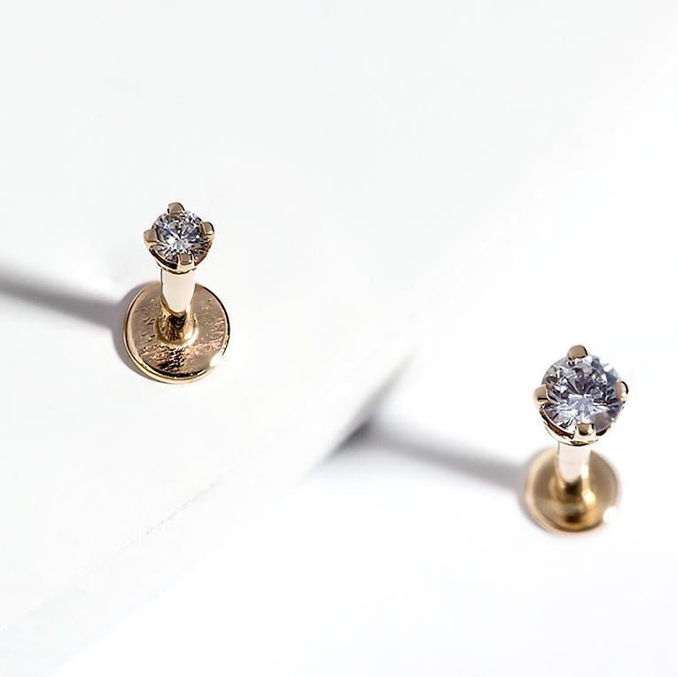 Two 14k yellow gold diamond basket-set flat back labret studs on white surface with soft shadows