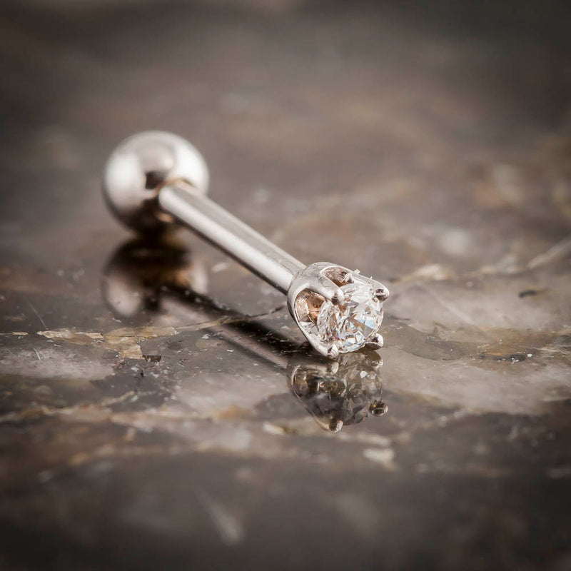 14k white gold 2mm CZ cartilage earring resting on stone surface, side profile showing post length