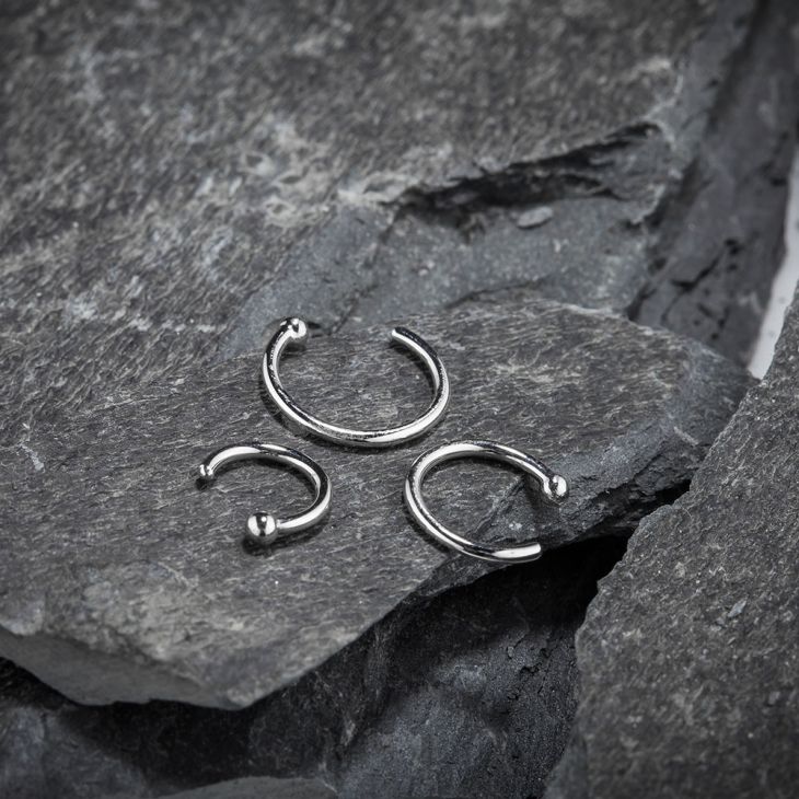 Three 950 platinum nose hoops in different diameters displayed on natural slate rock surface