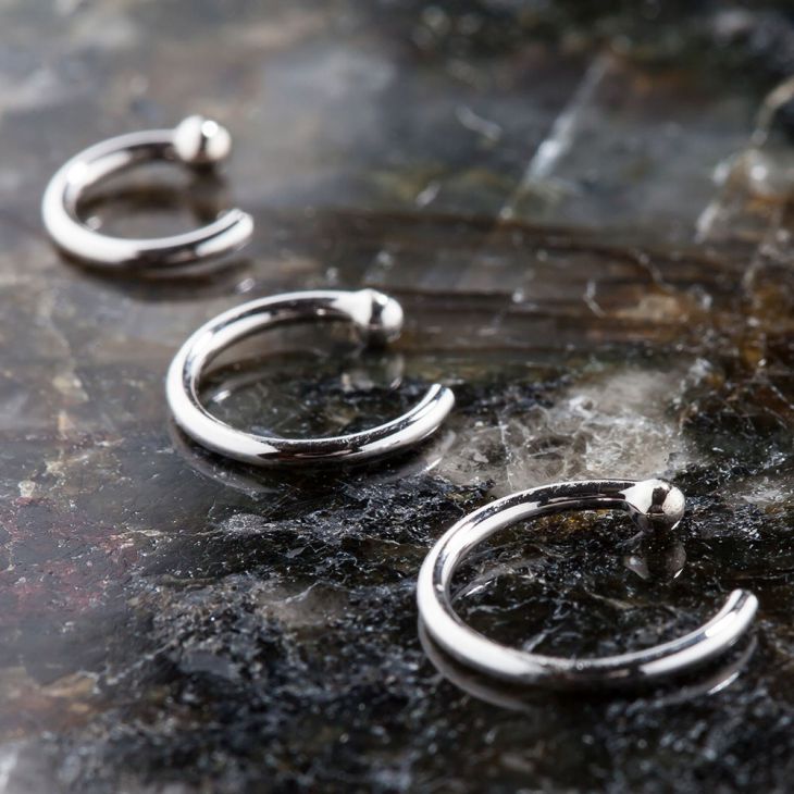 Three solid 950 platinum nose hoop rings in varying sizes arranged on dark stone surface