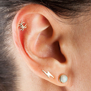 14K gold spider labret worn in a tragus piercing, styled with gold ear stack for scale