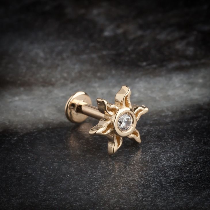 14K gold sunburst labret stud with CZ on dark stone surface, showing post and flat back disc