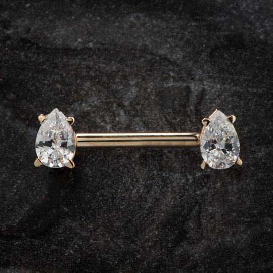 14K yellow gold straight barbell with clear pear-cut CZ ends, laid flat on dark stone surface