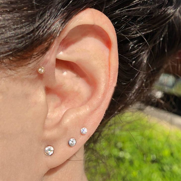 Multiple diamond bezel stud earrings in graduating sizes worn in lobe and cartilage piercings outdoors