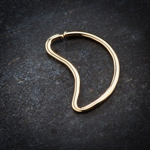 14K yellow gold moon-shaped seamless daith ring on dark stone surface, angled lifestyle view