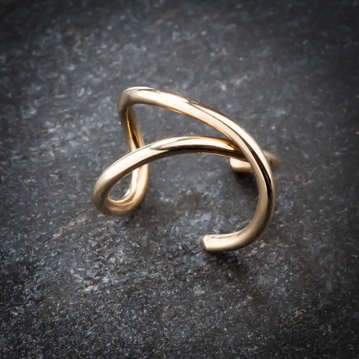 Angled side view of 14k yellow gold X band ear cuff resting on dark stone surface