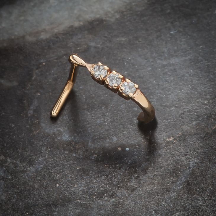 14K rose gold trinity diamond faux hoop nose ring resting on stone surface, angled lifestyle shot