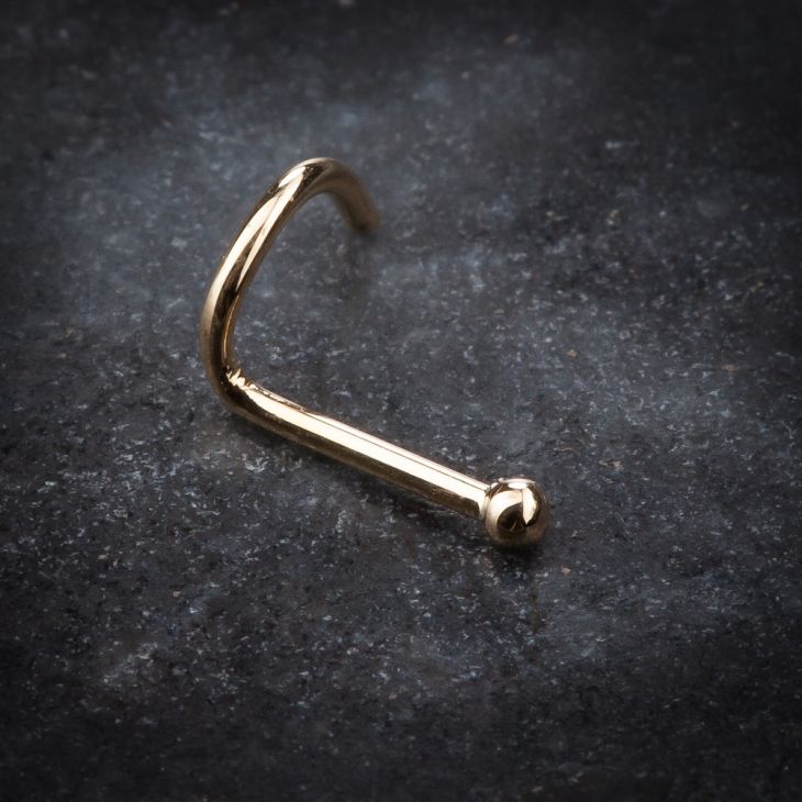 14K yellow gold tiny ball nose ring twist resting on dark stone surface, angled lifestyle view