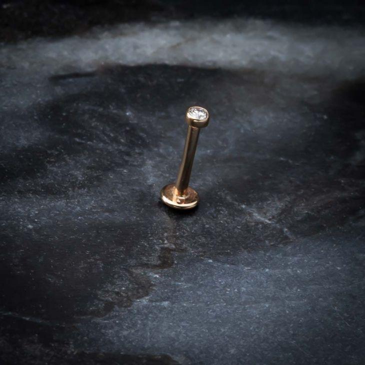 14k rose gold 2mm CZ bezel flat back labret standing upright on dark stone surface
