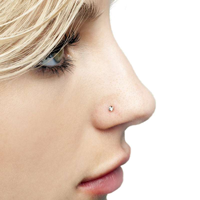 Close-up side profile of tiny diamond bezel threadless push pin end worn in model's nose piercing