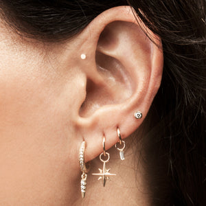 14k gold north star charm dangling from a hoop on a pierced ear, shown styled in a curated ear stack